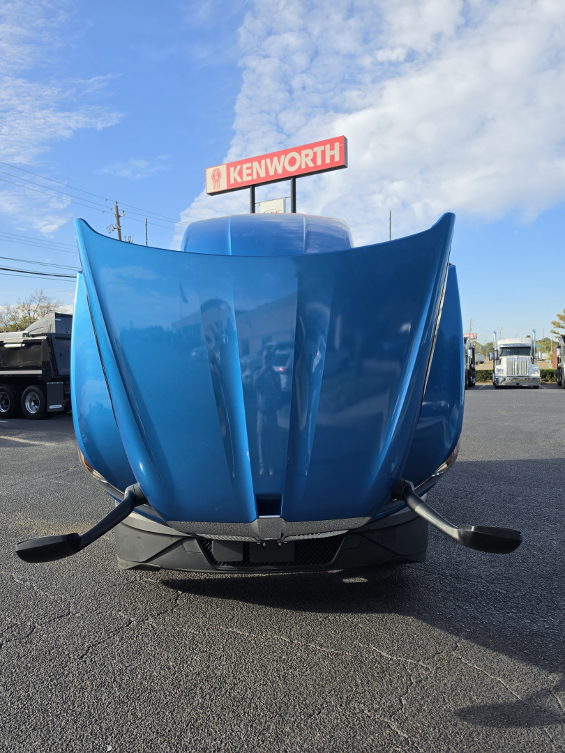 Blue Kenworth hood open showing front view of 2023 Kenworth T680 truck in a dealership lot.