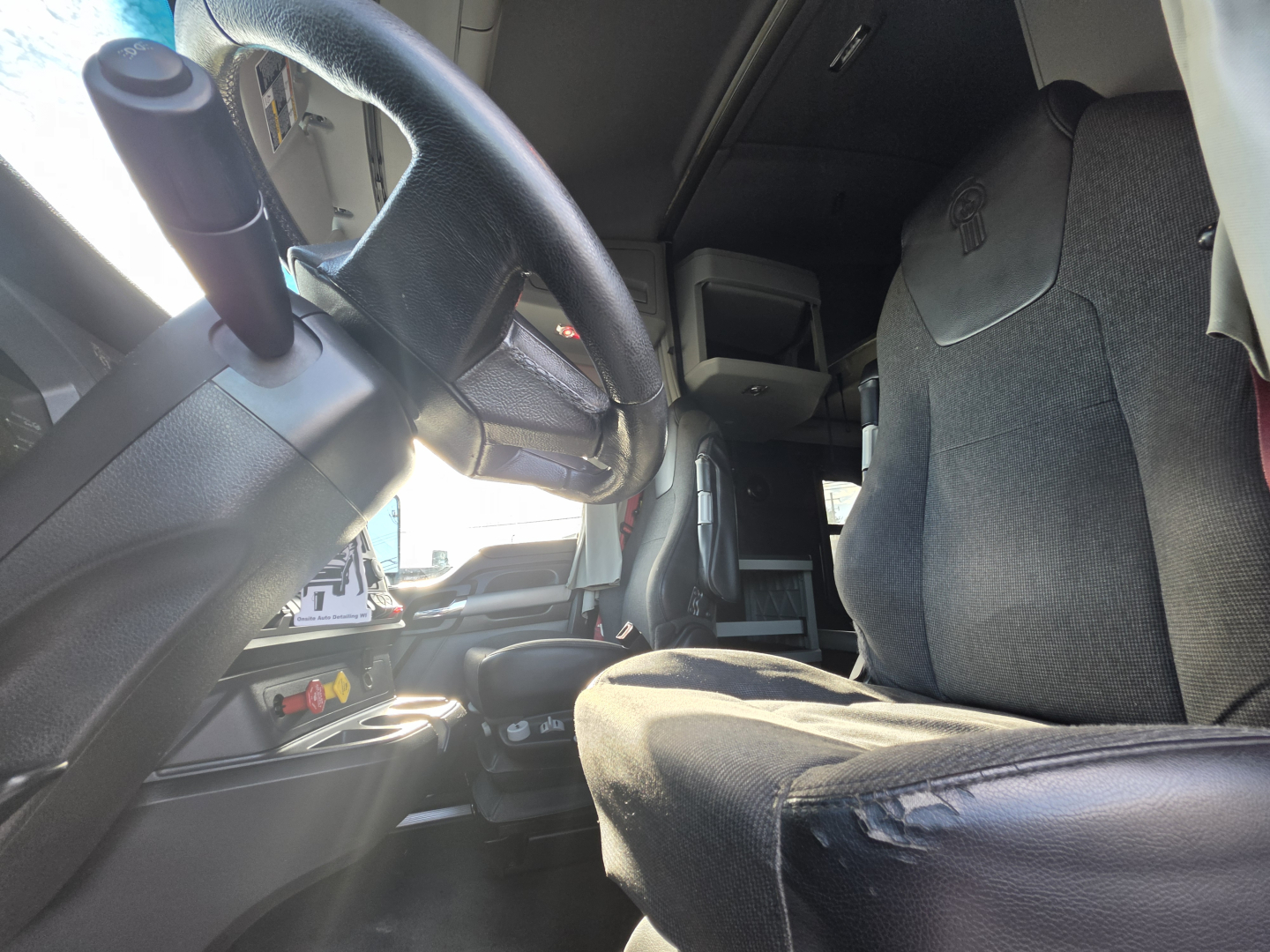 Kenworth T680 interior driver area showing steering wheel, dash, and front seat with fabric upholstery.