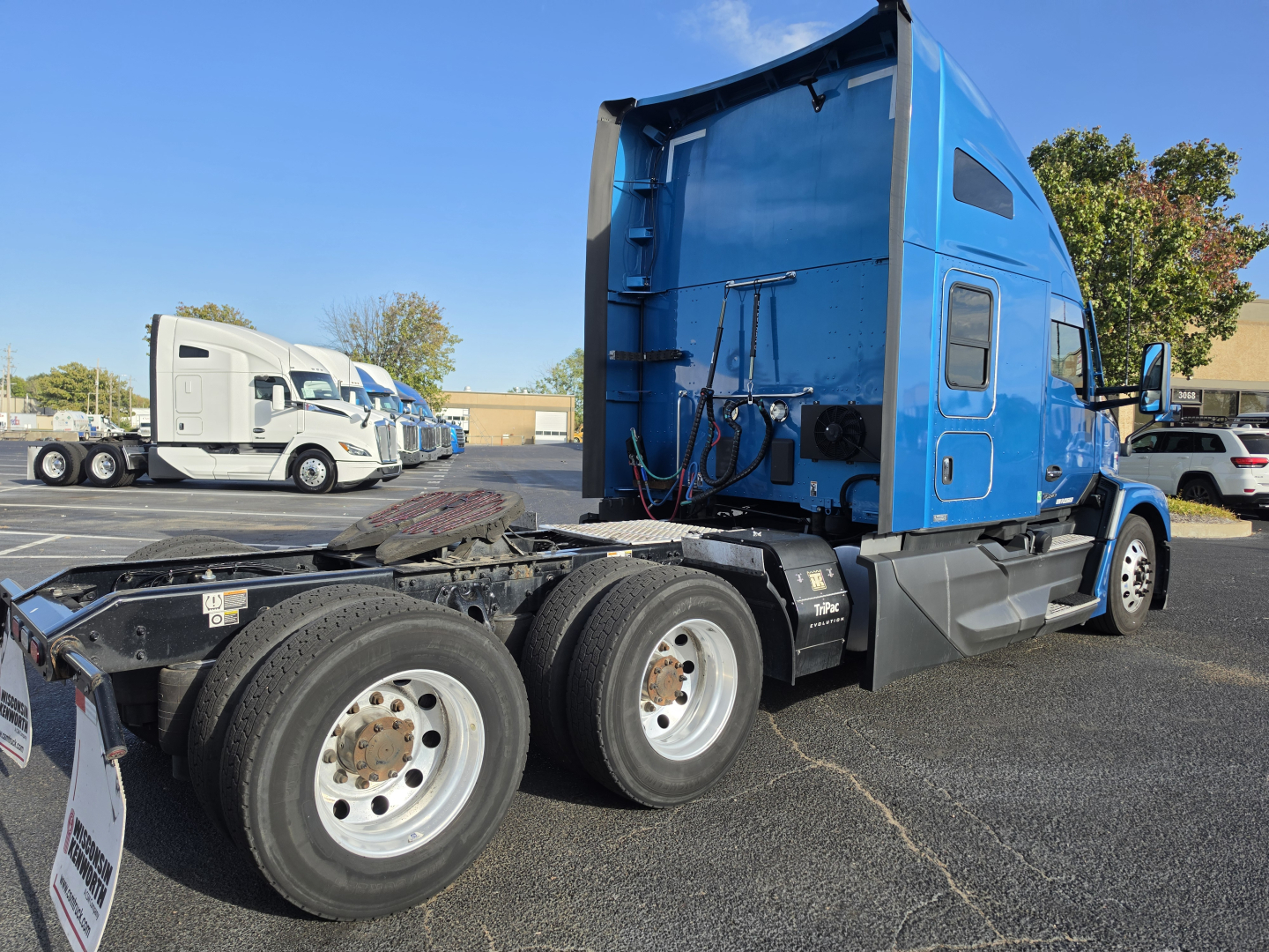 Kenworth T680 truck cab in blue, rear view of chassis showing dual rear axles and fifth wheel plate; other trucks in lot in background.