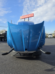 Blue Kenworth hood open showing front view of 2023 Kenworth T680 truck in a dealership lot.