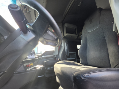Kenworth T680 interior driver area showing steering wheel, dash, and front seat with fabric upholstery.
