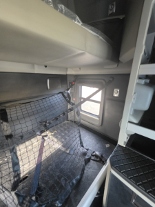 Kenworth T680 interior showing sleeper area and safety net, with side window and door frame visible.