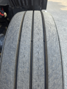 Kenworth T680 wheel/tire close-up showing tread wear on dual rear axle tires and part of chassis; no legible labels visible.