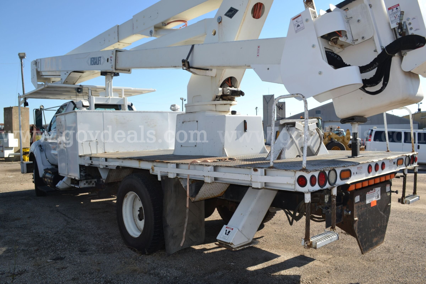 Ford F-750 bucket truck with raised aerial lift on a flatbed, rear view showing boom and stabilizers.