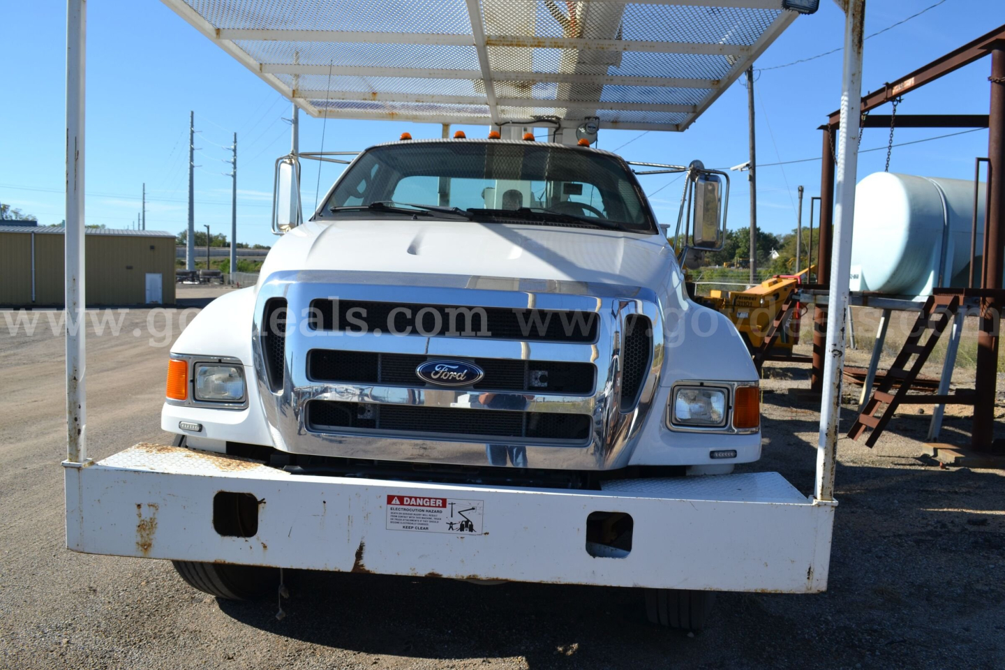 Front view of a white Ford bucket truck on a flatbed, with grille, headlights, and windshield visible. Text on bumper and license area faint. No other readable details.