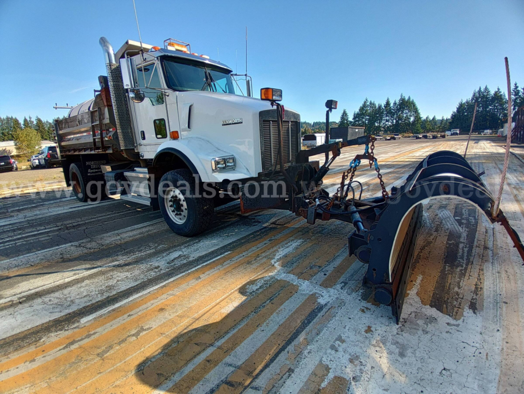Kenworth T800B dump truck front view showing front bumper, cab, and hitch with wheel and snow plow attachment.