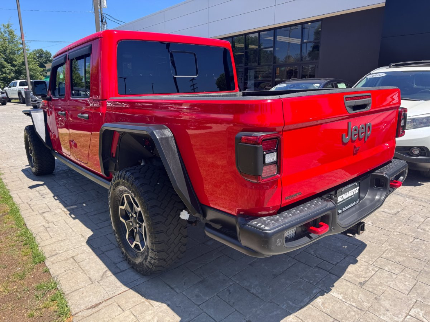 Red 2021 Jeep Gladiator pickup truck rear three-quarter view showing tailgate with Jeep badge and taillights, black bumper, and off-road tires.