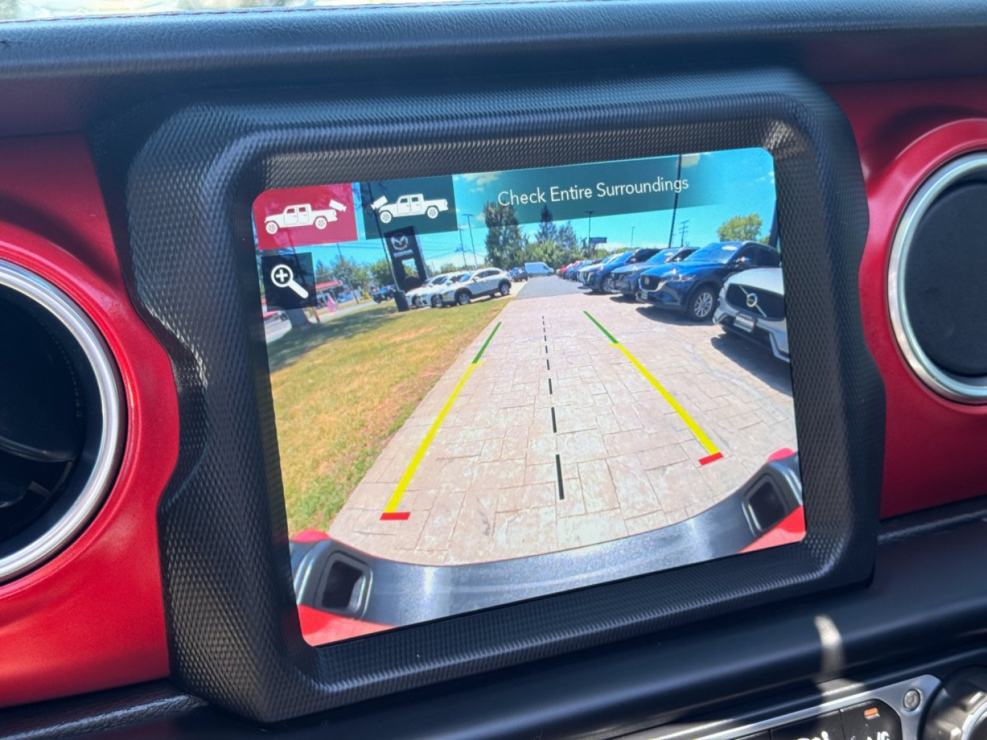 Jeep Gladiator rear view camera display showing backup guidelines and surrounding vehicles in a dealership lot.