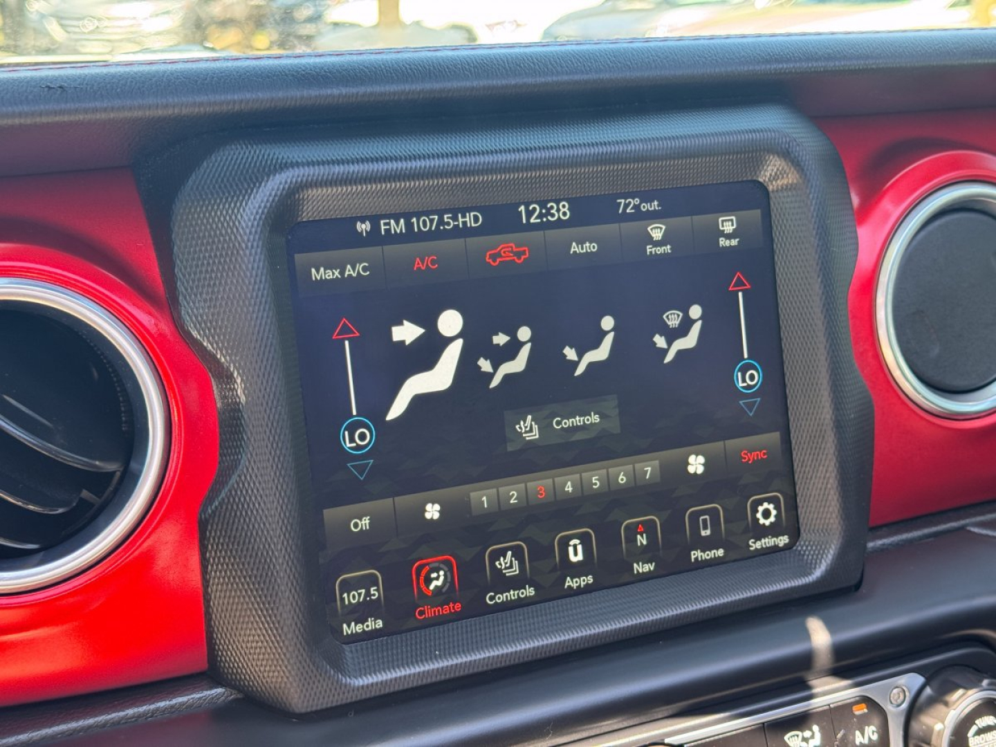 Center dashboard touchscreen in Jeep Gladiator showing climate controls and media icons in a red-accent cabin.