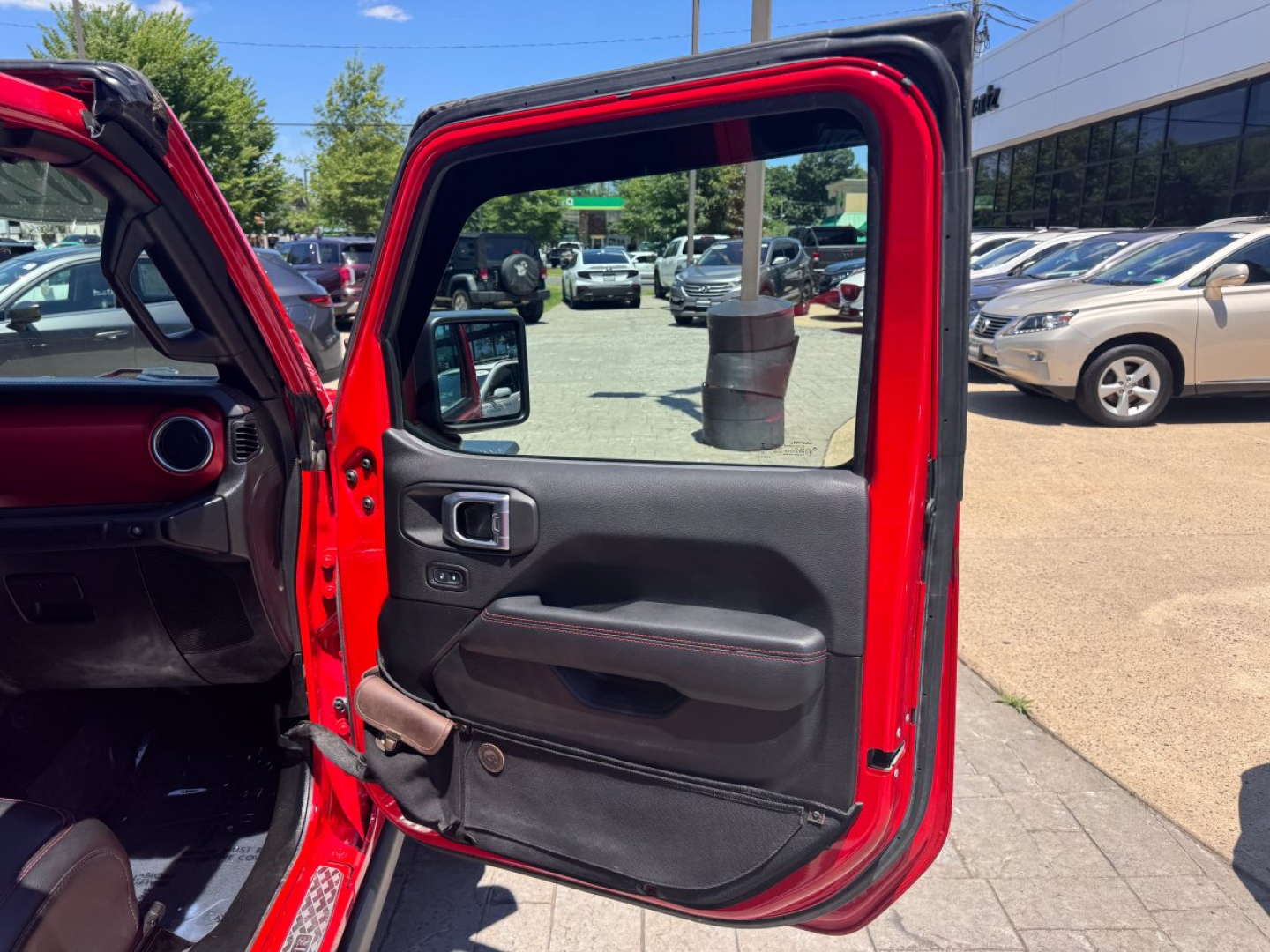 Jeep Gladiator interior door panel and open rear door showing red body, black door trim, and vehicle showroom lot in background.