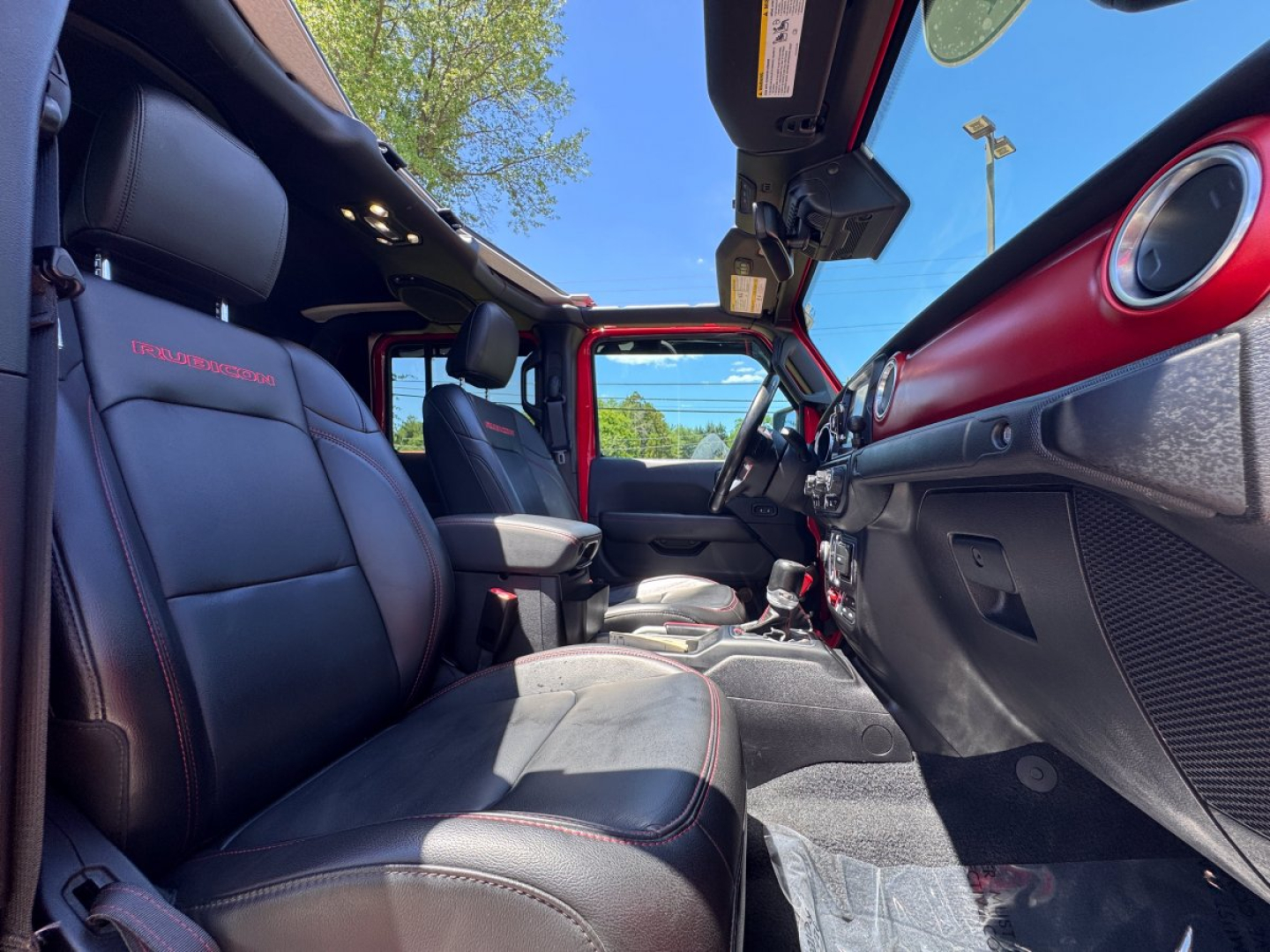 Interior of a 2021 Jeep Gladiator pickup truck with black leather seats, red stitching, and red dashboard accents; open roof and front seats visible.