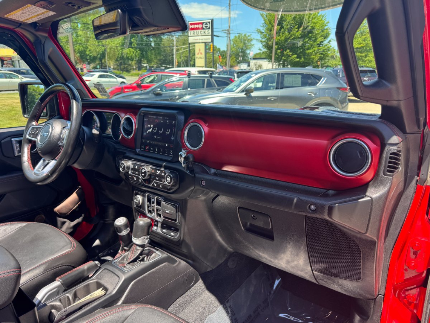 Interior of a 2021 Jeep Gladiator pickup truck showing red dashboard trim, steering wheel, center infotainment screen, circular vents, and gear shifter.