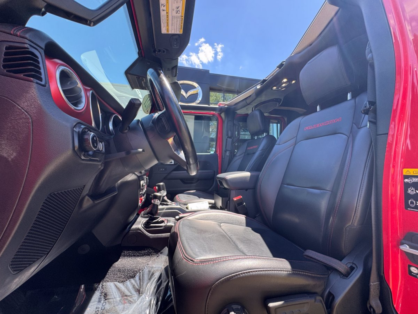 Interior of a red 2021 Jeep Gladiator showing front seats, steering wheel, dashboard, and center console. Visible features include red stitching on seats and AMG-like label on passenger seat.