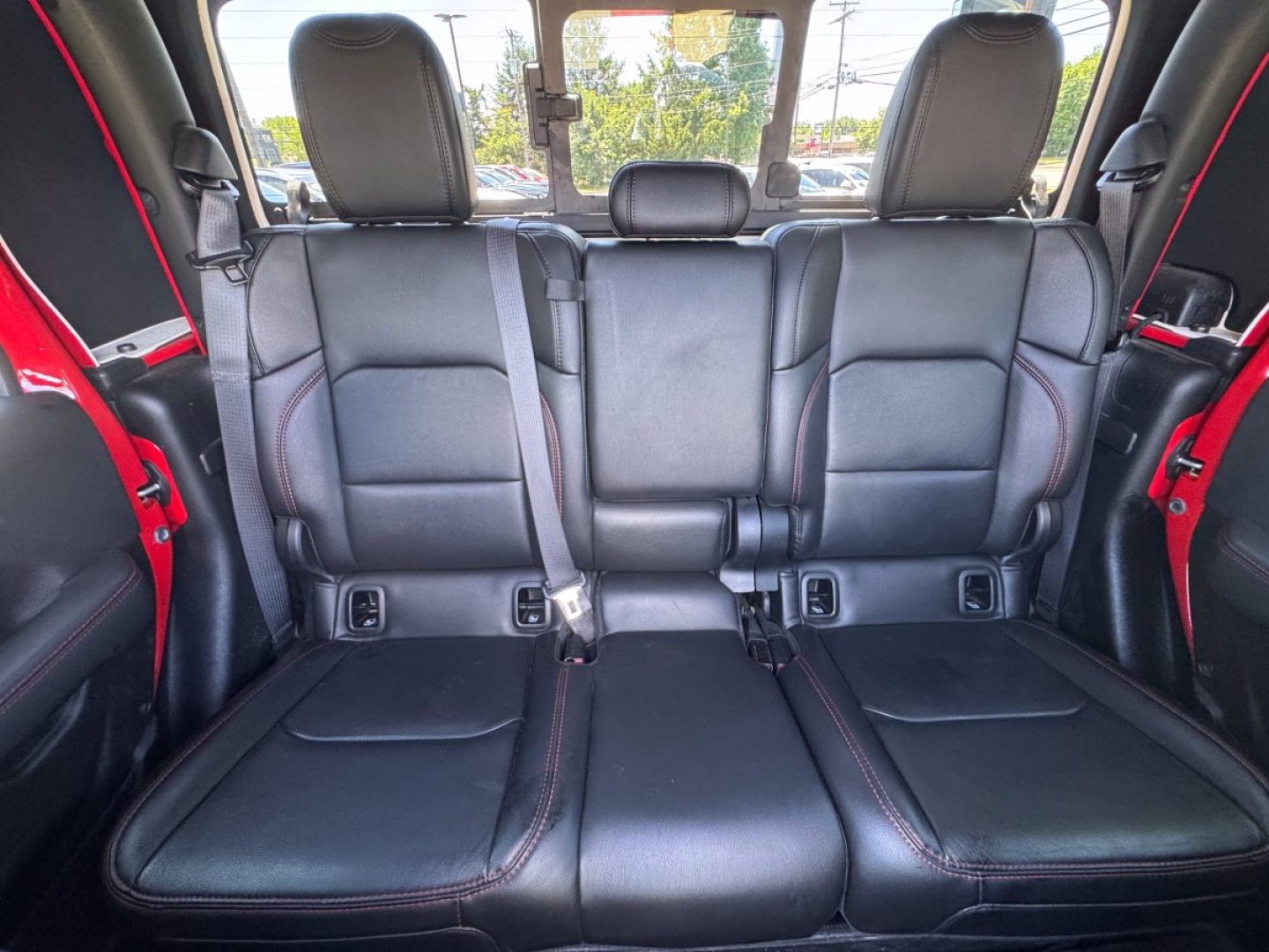 Jeep Gladiator rear 3-seat bench / back row shown in black leather upholstery with red stitching and seat belts visible