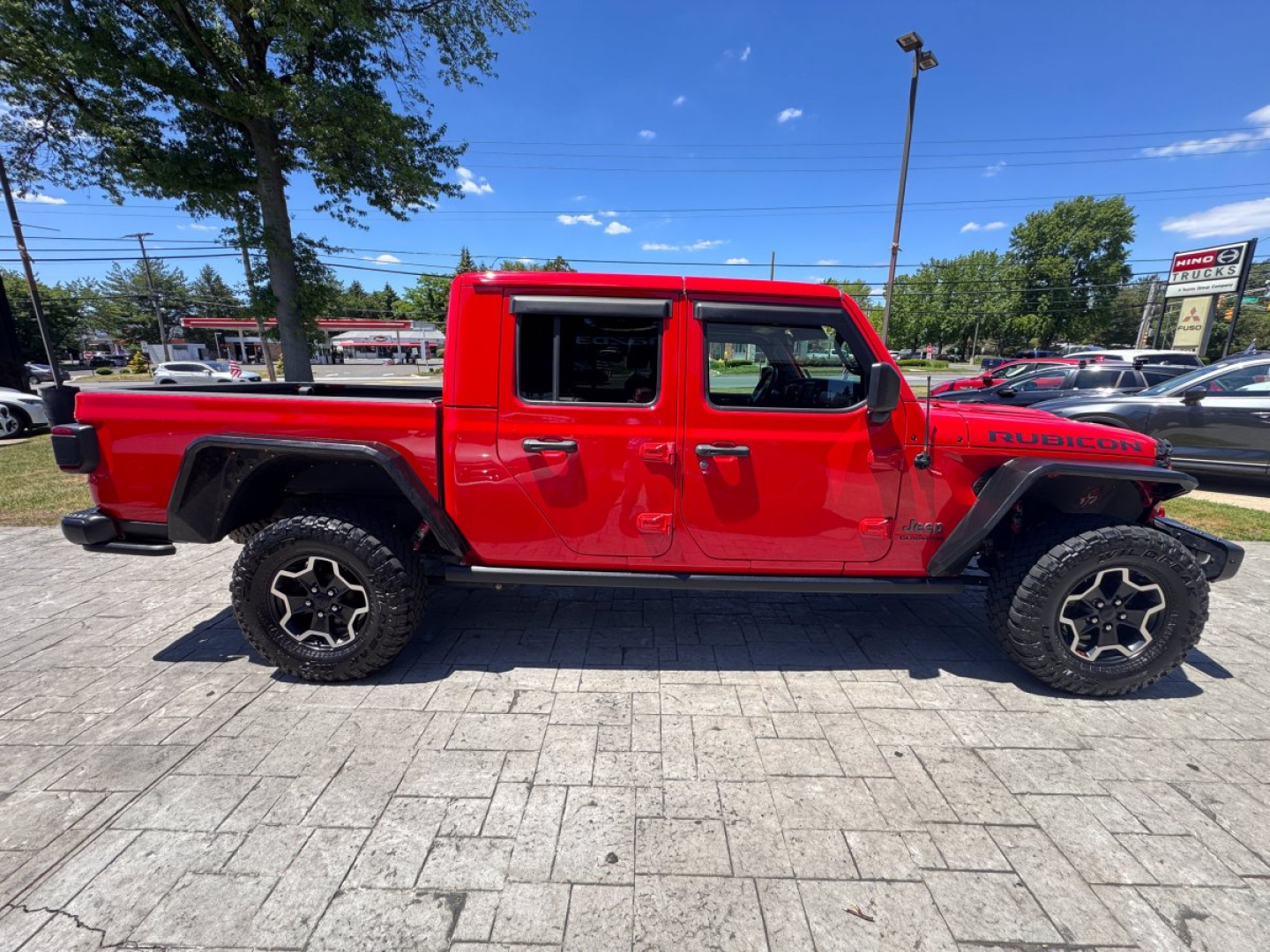 Jeep Gladiator pickup truck side view showing red exterior and Rubicon badge, four doors, large off-road tires.