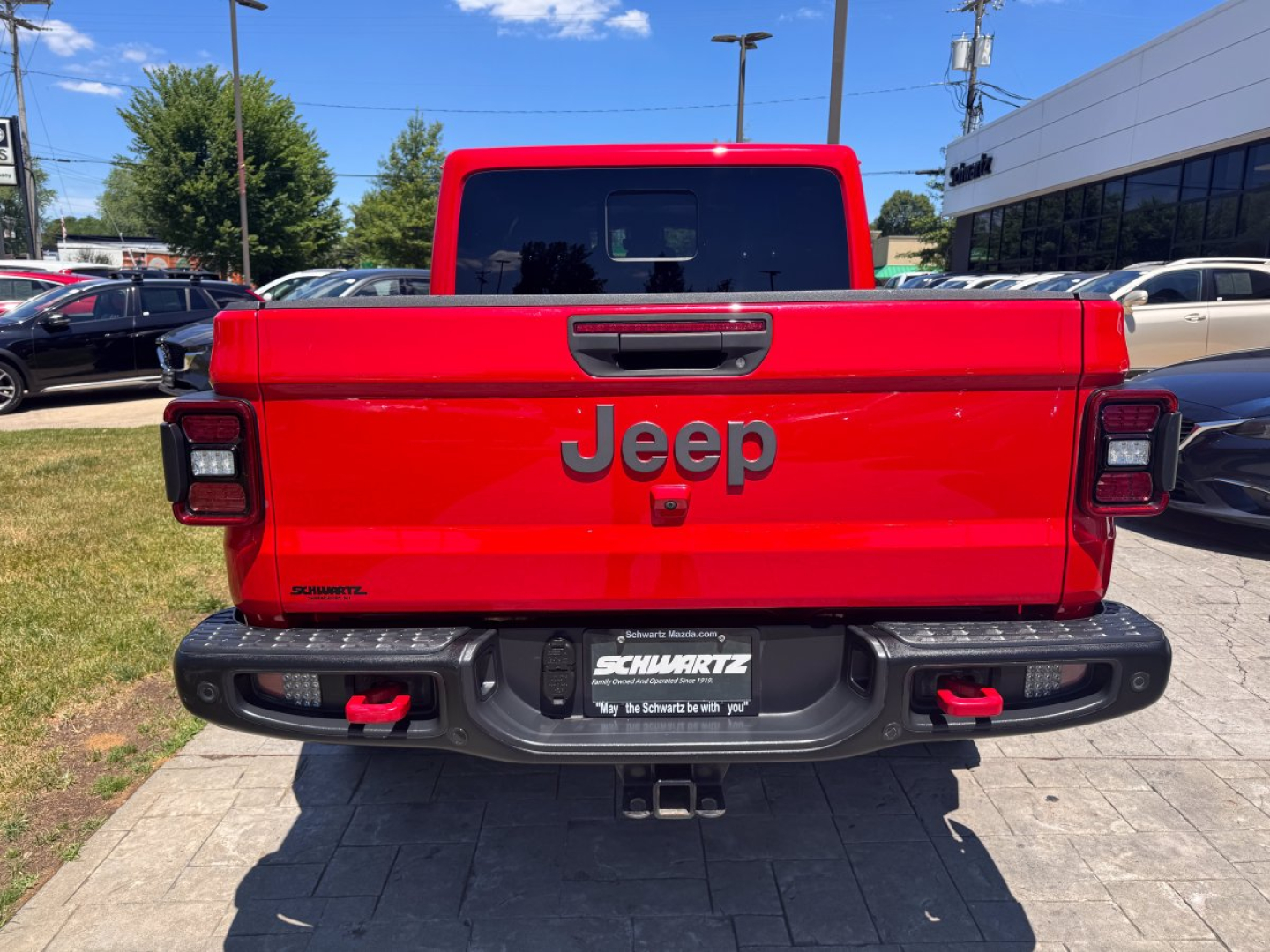 Jeep Gladiator tailgate with large Jeep logo and Schwarz license plate frame visible in rear view showing red truck bed.