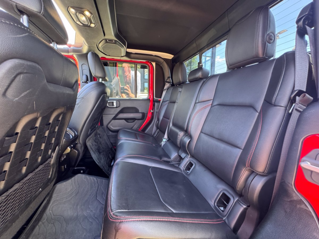 Jeep Gladiator interior rear seating area showing black leather seats with red stitching, rear door, and headrests.
