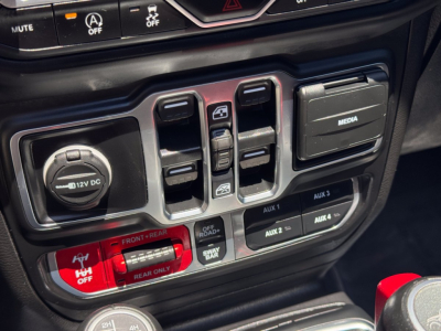 Truck interior center console with 12V DC socket and multiple auxiliary controls; visible text includes '12V DC' on the power outlet cap and 'AUX' labels on switches.