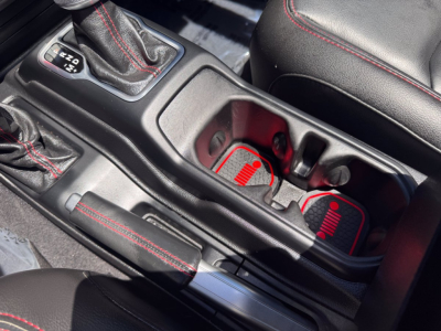 Jeep Gladiator center console area showing gear shifter with 4x4 options, cupholders, and red-trimmed seats in a used pickup truck interior.