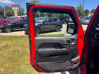 Jeep Gladiator door panel and open red door in foreground with dealership lot in background.