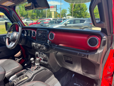 Interior of a 2021 Jeep Gladiator pickup truck showing red dashboard trim, steering wheel, center infotainment screen, circular vents, and gear shifter.
