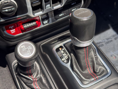 Jeep Gladiator interior showing shifter and transfer case lever with red-stitched leather boots and dashboard controls.