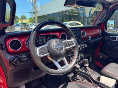 Jeep Gladiator interior view showing steering wheel with Jeep emblem, red dashboard accents, and center console gear shifter