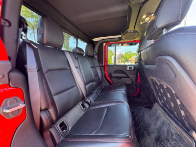 Jeep Gladiator rear seating area with black leather seats and red stitching, interior cabin view through open rear door.