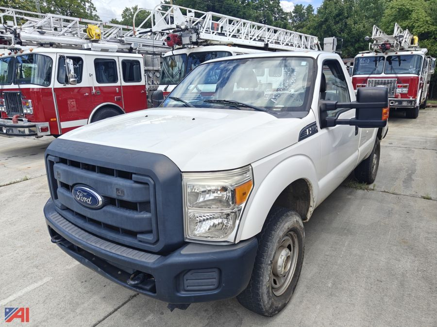 Ford F-250 pickup truck in a lot with fire trucks in background, white cab with black grille and bumper, steel wheels, N/A on this model.