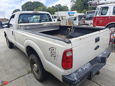 Ford F-250 pickup truck rear view showing bed with toolbox and 4x4 badge, white and worn tailgate, in a used truck lot.