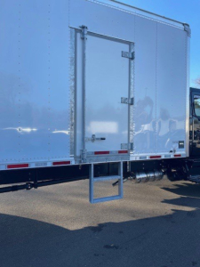 Box van truck rear/side showing cargo door with hinges, rear step, and reflective stripe along box edge.