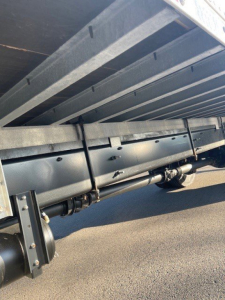 Underbody view of a box van truck showing suspension and frame rails with a cylindrical component and leaf spring hardware.