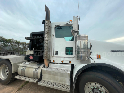 Kenworth T800 cab view showing chrome fuel tanks, side step, and exhaust stack; front wheel and part of sleeper cabin visible.