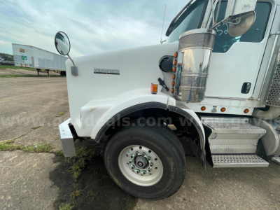 Kenworth T800 front-left view showing wheel, fender, and side mirror with 'KENWORTH' emblem on hood and chrome fuel tank; clear sky.