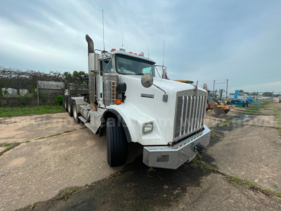 Kenworth T800 truck front-left view with large chrome grille and dual exhaust stacks, white cab, daytime outdoor lot.