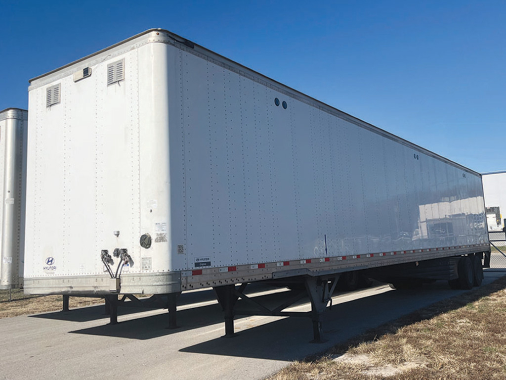 Trailer side view showing high-cube aluminum Hyundai trailer with tandem axles and rear access doors, white exterior, no visible branding text.