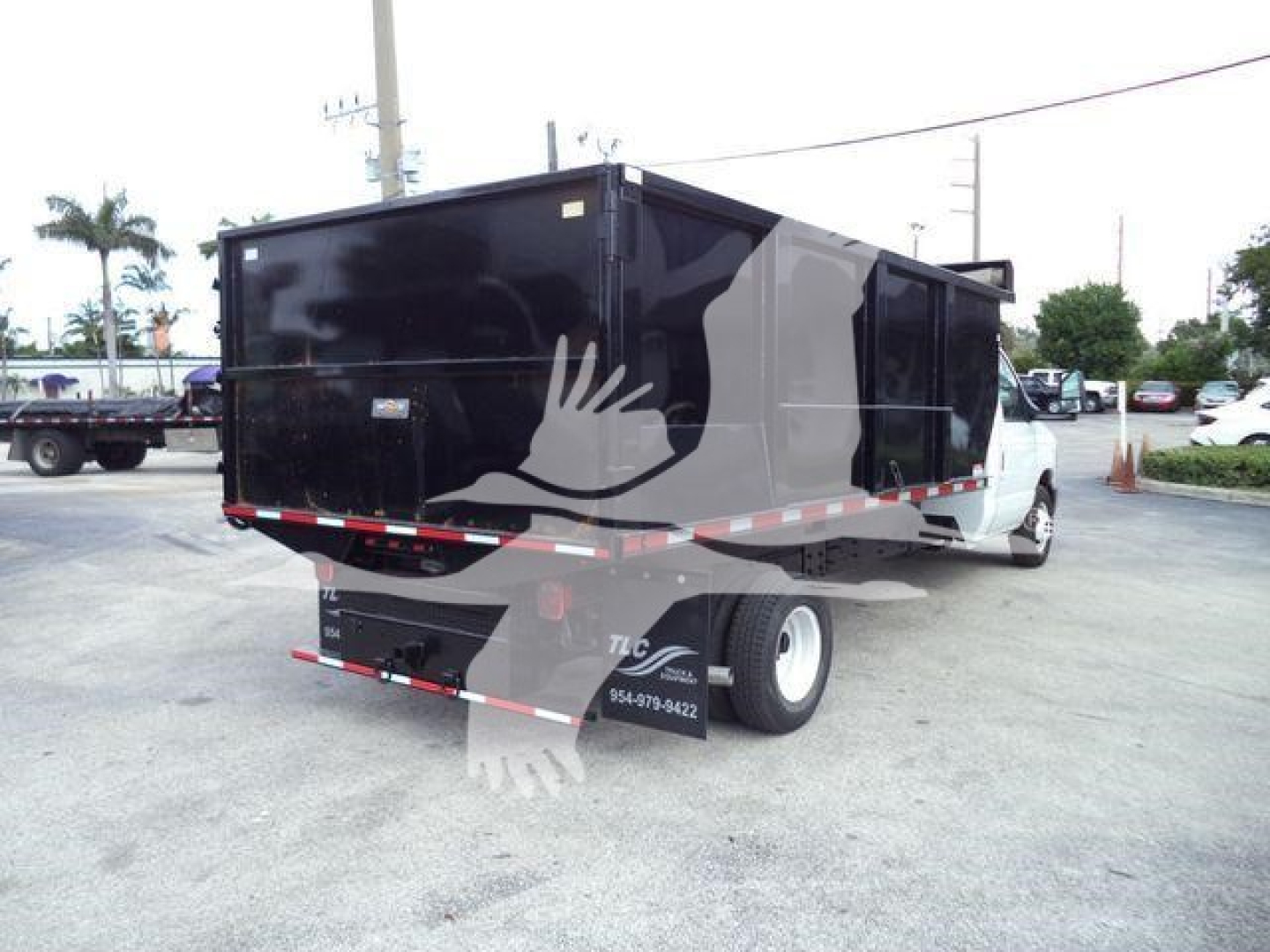 Dump truck body mounted on a Ford E-450 chassis seen from rear three-quarter view with a black dump bed and white cab.