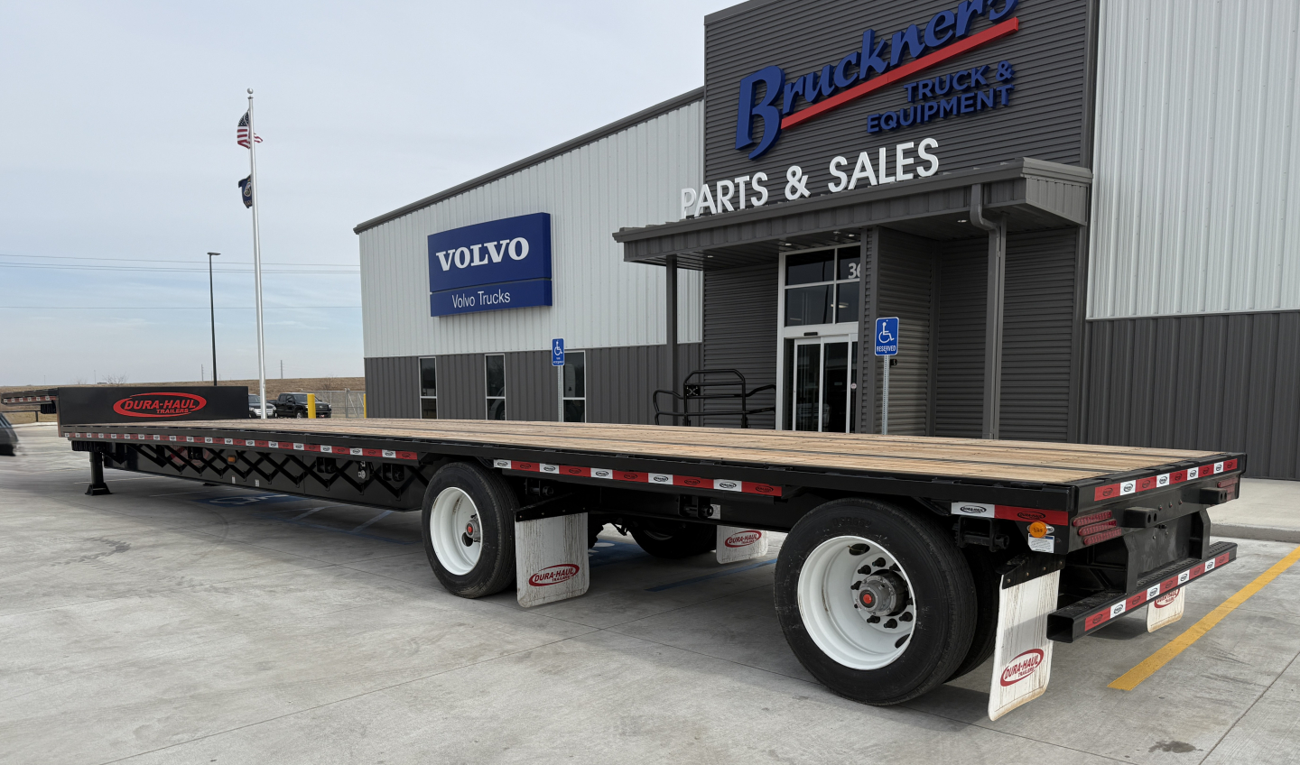 Trailer showing 53' drop deck flatbed with dual rear axles at a truck dealership lot.