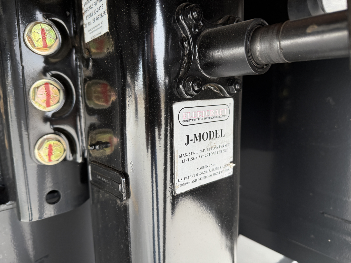Hydraulic jack and control valves with a J-model label on a black trailer support beam.