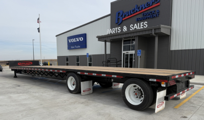 Trailer showing 53' drop deck flatbed with dual rear axles at a truck dealership lot.