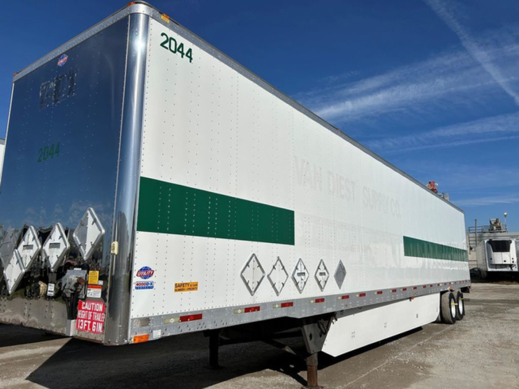Trailer side view showing 2044 markings and hazard placards on a white dry van trailer with green stripe.