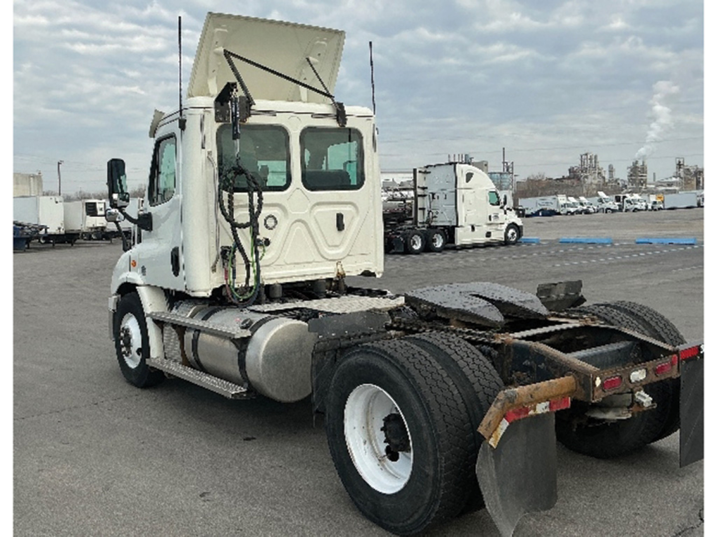 Truck cab and chassis showing rear sleeper area, Freightliner Cascadia 113 style, white with dual rear axles and exposed hitch, daytime lot with other trucks in background.