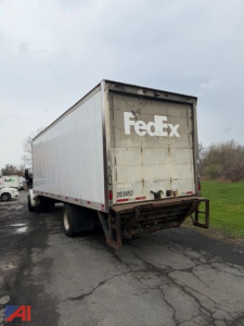 Box truck rear view showing FedEx-branded trailer with closed white cargo box and dark dock bumper. License/ID tag 203457 visible on rear. Overcast sky and road surface.