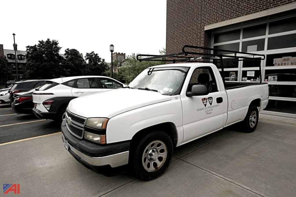 Chevrolet Silverado 1500 pickup truck in white with ladder rack and decals on the door, parked outside a building.