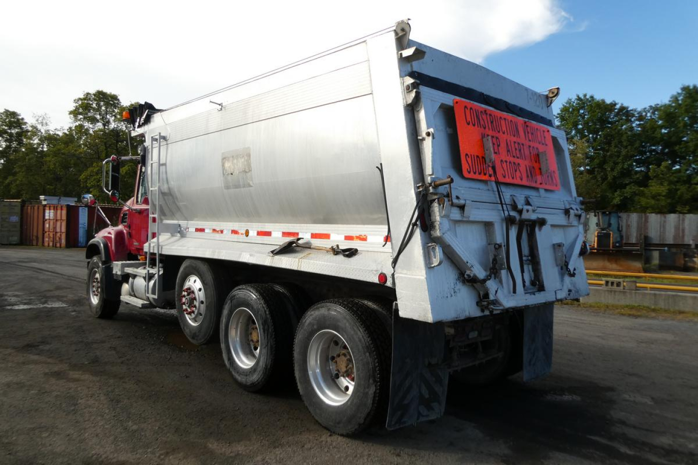 Dump truck rear and side view of a 2005 Mack CV Granite CV713 dump truck with a large metal dump bed and orange caution sign on the back.