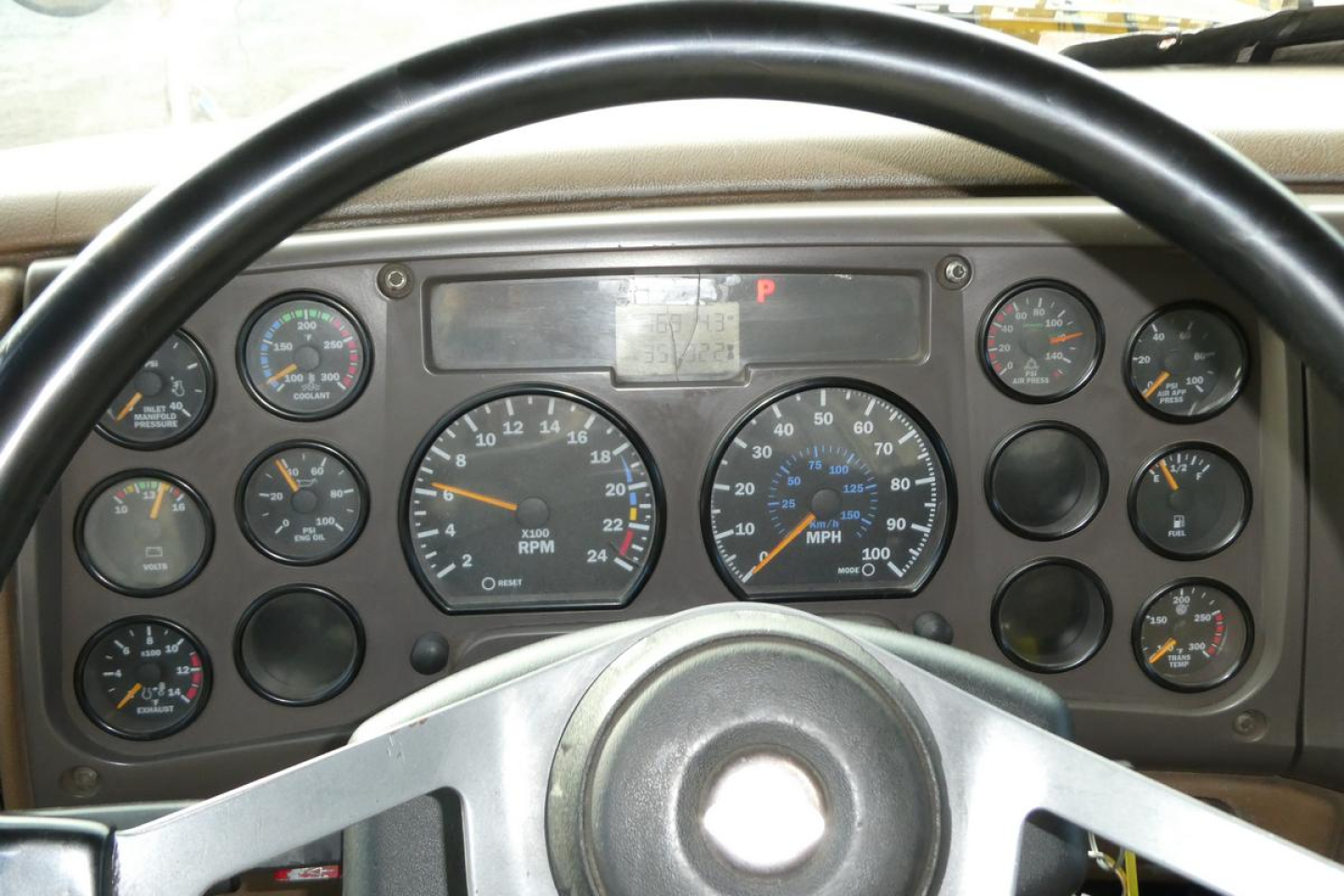 Dashboard view of a Mack CV Granite truck showing multiple gauges and steering wheel, with central tachometer and speedometer, various indicator lights.