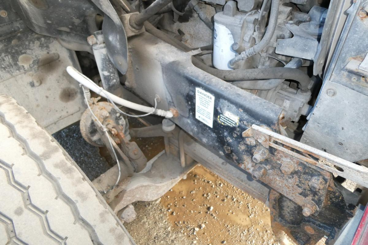 Truck frame and front suspension of a 2005 Mack CV (Granite) CV713 dump truck showing chassis, fuel lines, and wheel well. Visible label panels and rust/dirt on underbody.