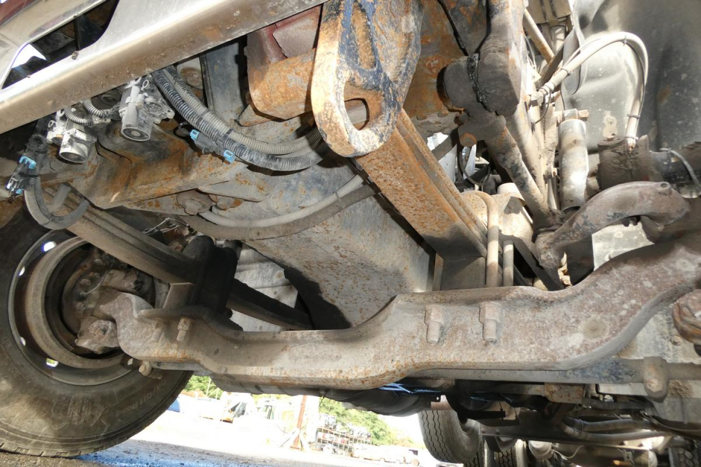 Underbelly view of a Mack CV Granite truck showing front suspension components and rusty frame member.