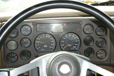 Dashboard view of a Mack CV Granite truck showing multiple gauges and steering wheel, with central tachometer and speedometer, various indicator lights.
