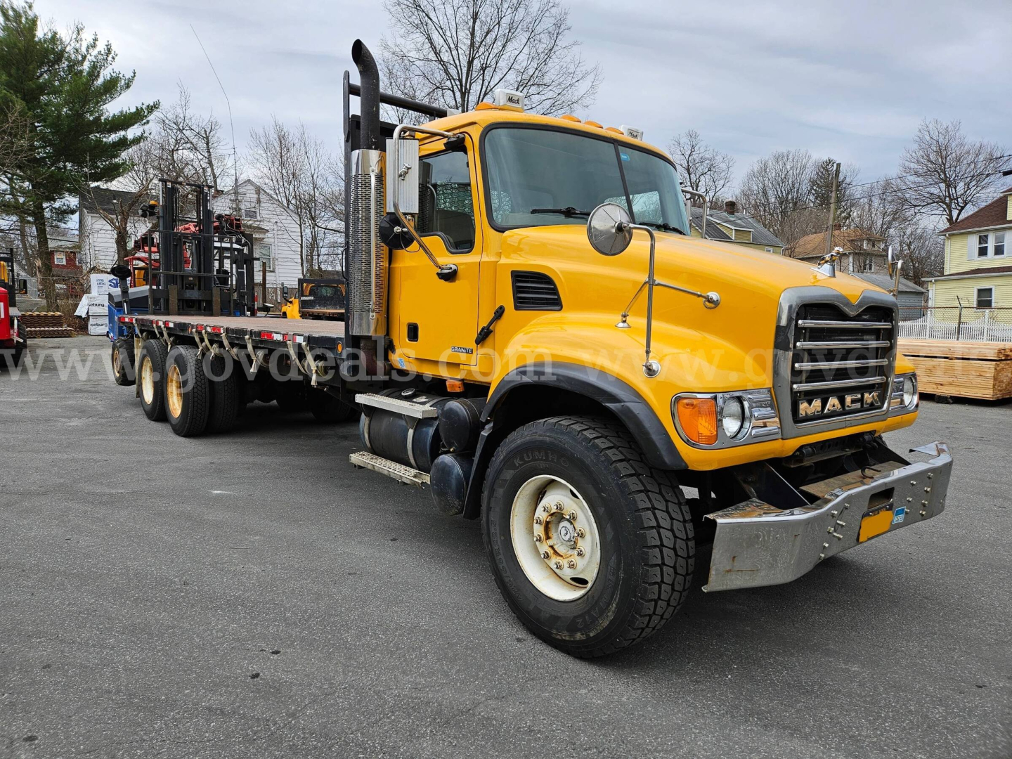 Yellow Mack CV713 heavy duty truck in flatbed setup, Cab front view with bumper, grille, and dual rear wheels visible.